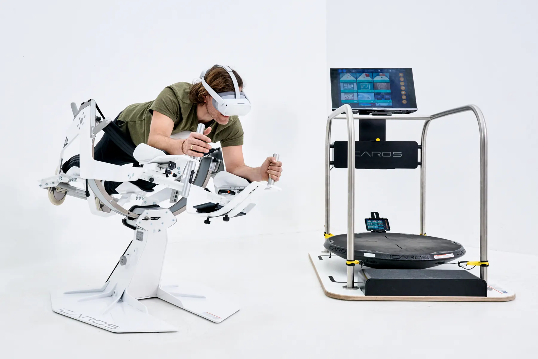 Ein Mann trainiert mit VR-Brille auf dem ICAROS Health, daneben steht der ICAROS Guardian mit Bildschirm